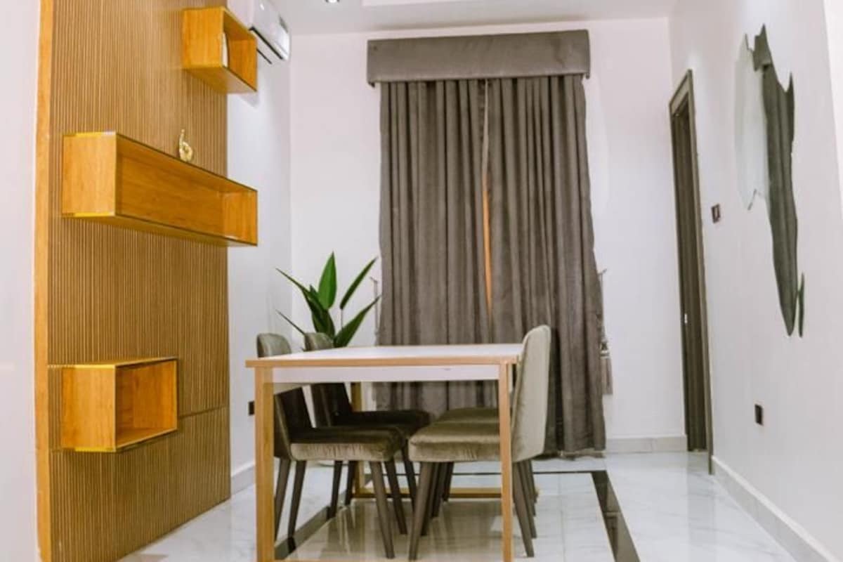 A modern dining area with a white table and chairs, a wooden accent wall, and a grey curtain.