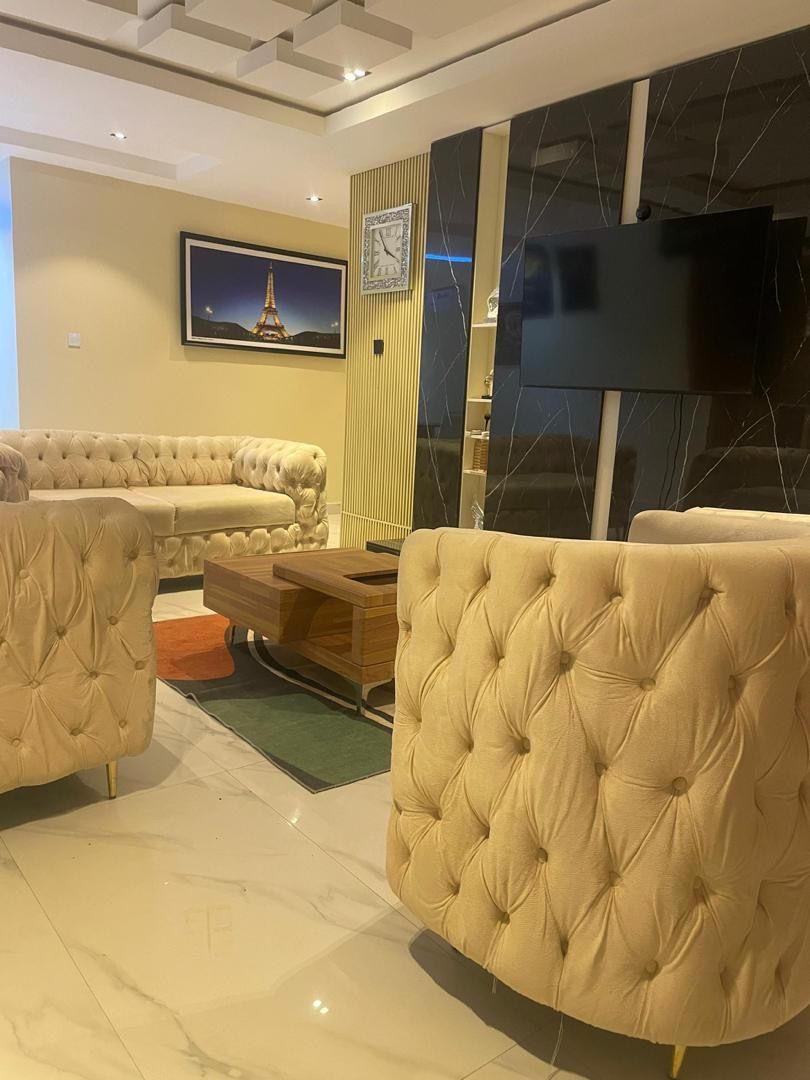 A modern living room with a large sofa set, a coffee table, and a flat-screen TV mounted on the wall.