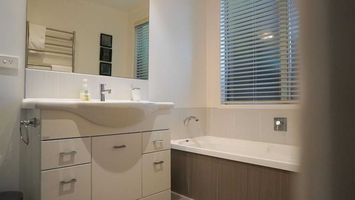 Ein Badezimmer mit einem weißen Waschbecken, einem Spiegel und einem Fenster mit Jalousien.