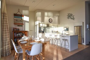 A modern kitchen with a central island, bar stools, and a dining area with a wooden table and chairs. - Lakefront Oasis - Jetty, Hot Tub & Kayaks (Okere Falls)
