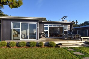 Una casa moderna amb una ampla porta corredissa de vidre, una terrassa amb mobiliari exterior i un cel serè.