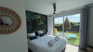 A bedroom with a bed, a large window, and a view of a garden.