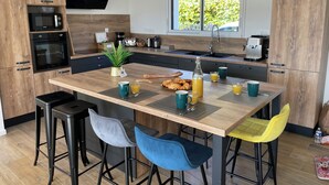 A modern kitchen with wooden cabinets, a central island with bar stools, a TV mounted above the island, and a window providing natural light.