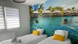 A room with two beds, each with white bedding and a yellow pillow, and a mural of a tropical beach scene.