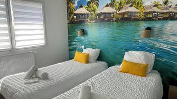 Een kamer met twee bedden, elk voorzien van wit beddengoed en een geel kussen, en een muurschildering van een tropisch strand.