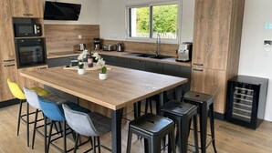 A modern kitchen with wooden cabinets, a central island, bar stools, and a built-in oven.