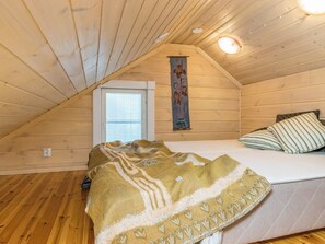 Um quarto de sótão acolhedor com teto inclinado, uma cama com travesseiro listrado, um cobertor e uma tapeçaria decorativa.
