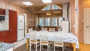Interior de una cabaña de madera con comedor, cocina y ventanas amplias.