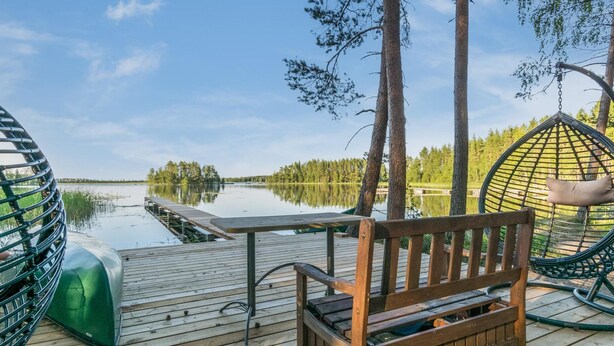 Una terraza de madera con un banco y una silla colgante, con vista a un lago tranquilo.