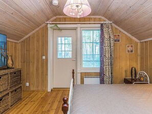 Une chambre avec des murs en bois, un lit, une fenêtre avec des stores, une porte et un luminaire suspendu.