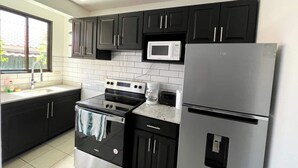 A modern kitchen with dark cabinets, a stainless steel refrigerator, a microwave, an oven, and a coffee maker. - Charming Condo Orchidea (Playas Del Coco)