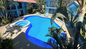 A resort with a large swimming pool surrounded by palm trees and blue buildings. - Charming Condo Orchidea (Playas Del Coco)