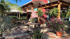 An outdoor patio area with tables and chairs, surrounded by potted plants and palm trees. - Charming Condo Orchidea (Playas Del Coco)