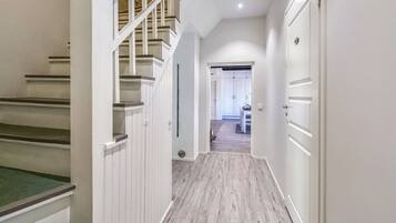 A hallway with a wooden staircase, a door with a handle, and a light switch on the wall.