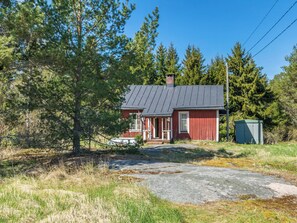 Ein rotes Holzhaus mit einem Metall-Dach, umgeben von Bäumen und einer Rasenfläche.