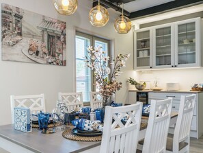 Una cocina moderna con armarios blancos, una mesa de comedor con vajilla azul y blanca, y un cuadro grande con motivos florales en la pared.