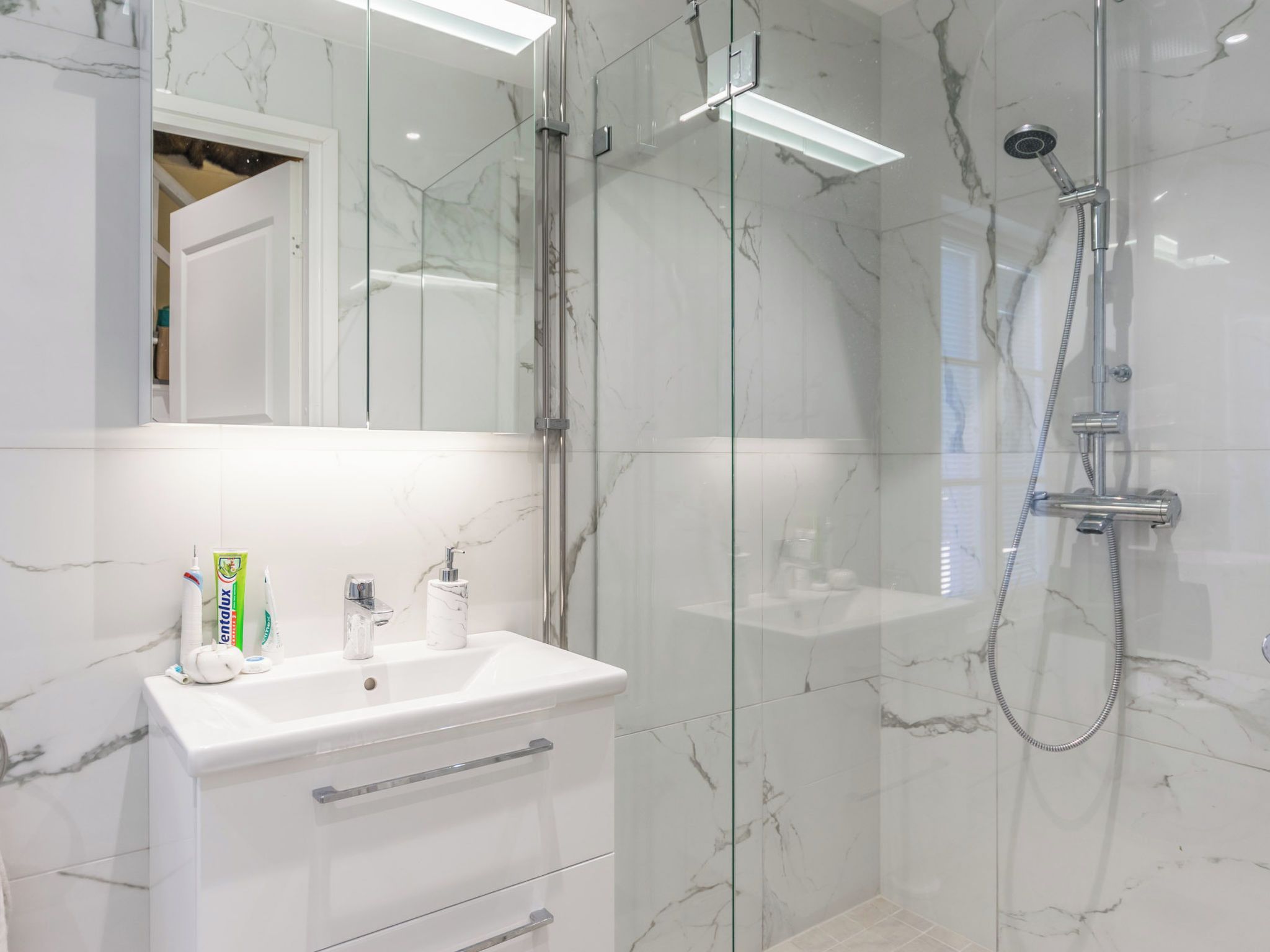 Un bagno moderno con cabina doccia in vetro, piastrelle in marmo bianco e un mobile lavabo con articoli da toilette.