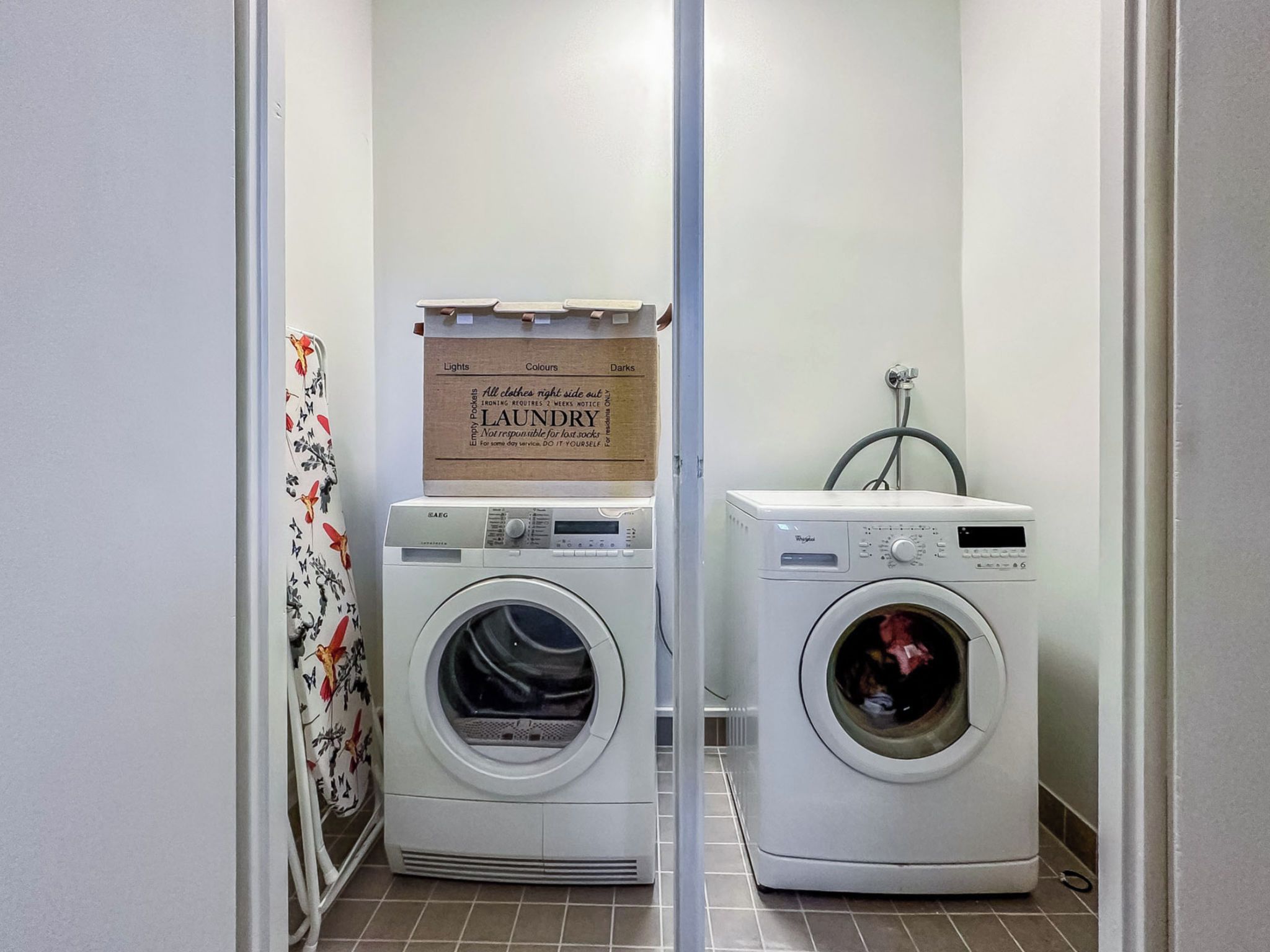 A laundry room with two front-loading washing machines, a drying rack, and a sign above the machines.