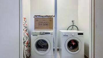 A laundry room with two front-loading washing machines, a drying rack, and a sign above the machines.