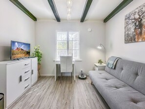 Una sala de estar moderna con un sofá gris, un escritorio con una silla, un televisor y una ventana con persianas.