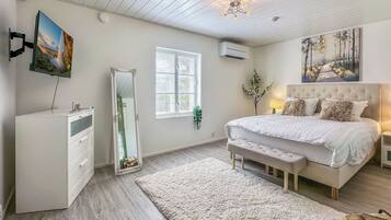 Une chambre à coucher avec un lit, des tables de chevet, un miroir, une commode, une fenêtre et un tableau accroché au mur.