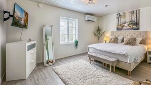 A bedroom with a bed, a bedside table, a mirror, a window, and a painting on the wall.