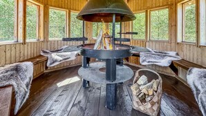 A wooden cabin with a central wood stove, benches, and a basket of firewood.