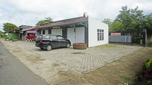 Un edificio pequeño con un coche estacionado frente, un camino de entrada pavimentado y un acceso con portón.