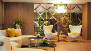 Een moderne woonkamer met een bank, twee witte fauteuils, een ronde salontafel en een decoratieve roomdivider met een kroonluchter.