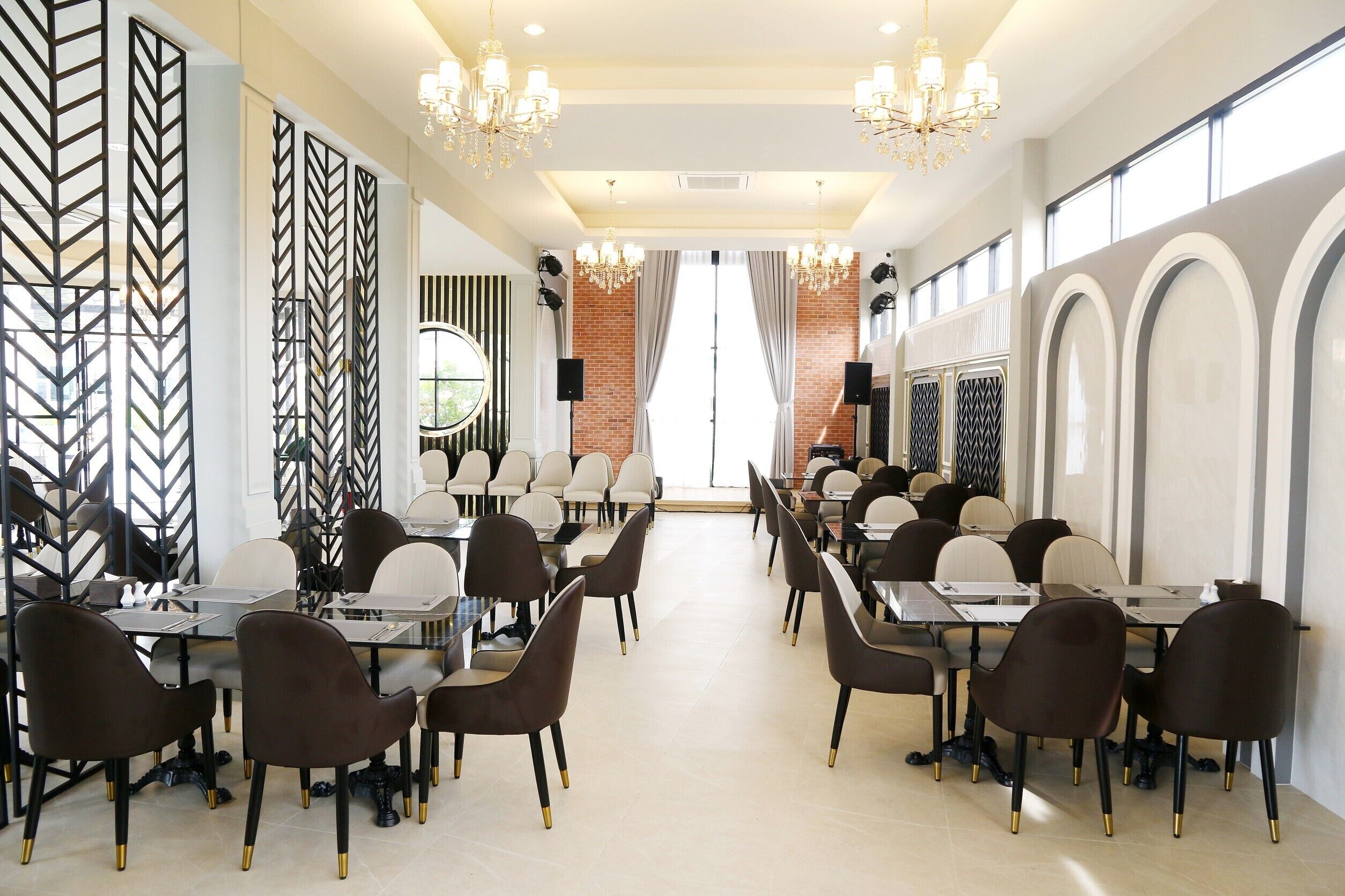 A spacious dining area with long tables and chairs, chandeliers, and brick walls.