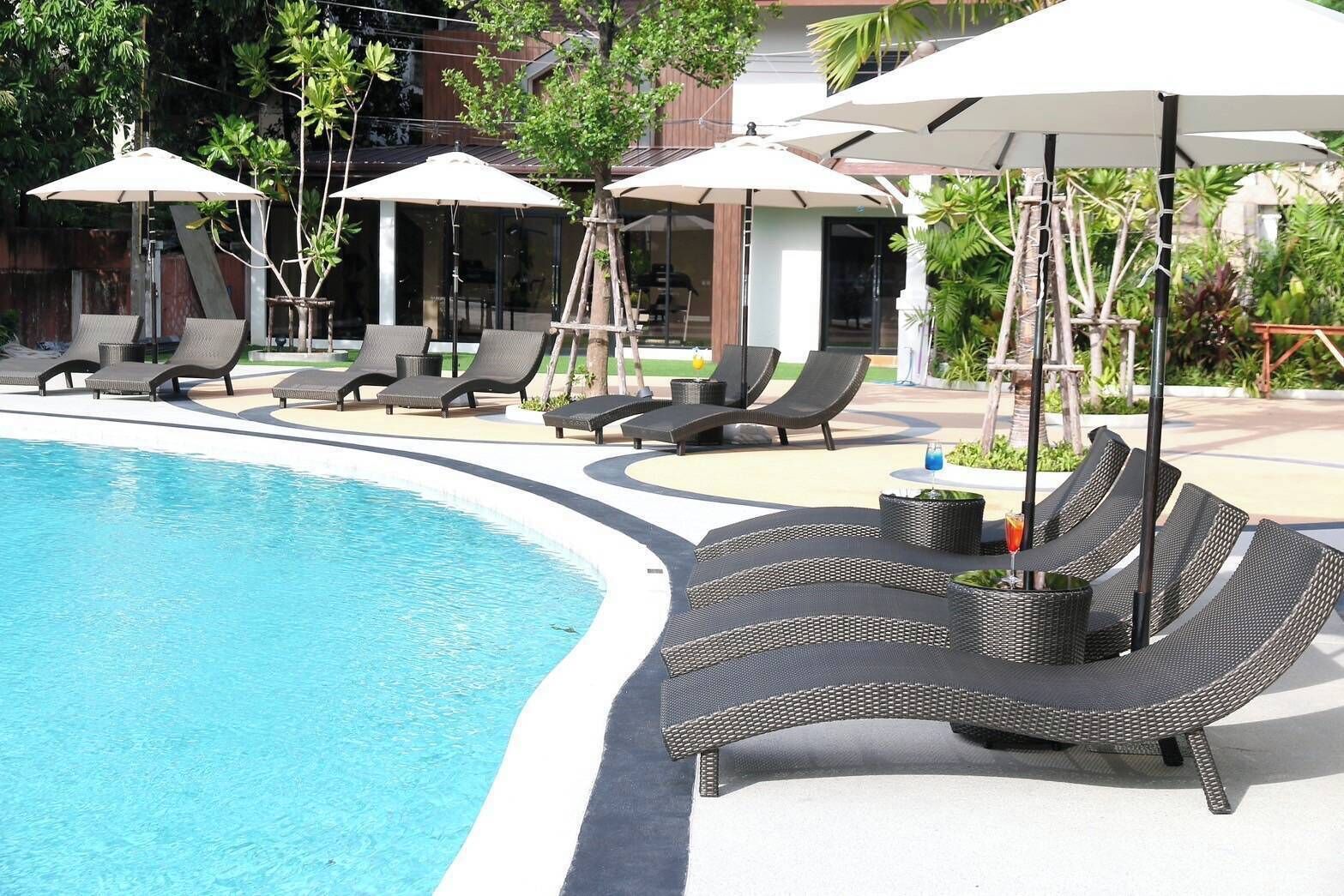A poolside area with lounge chairs and umbrellas, surrounded by greenery and a building in the background.