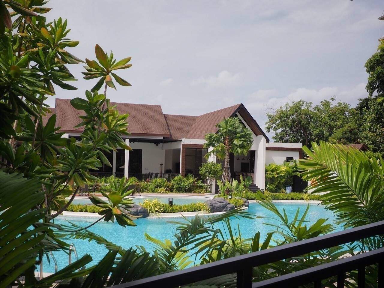 A modern hotel with a swimming pool surrounded by lush greenery.