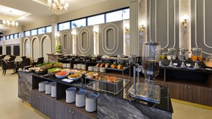 Een buffetopstelling met diverse gerechten, een koffieapparaat en een zithoek met tafels en stoelen.