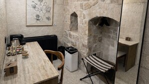 Une pièce aux murs de pierre, avec une table en bois, une chaise, une œuvre d’art florale encadrée, un grand miroir et un radiateur.