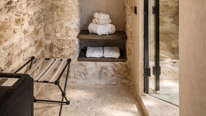 Une salle de bain aux murs en pierre, avec un banc, une étagère pour les serviettes et une porte de douche en verre.