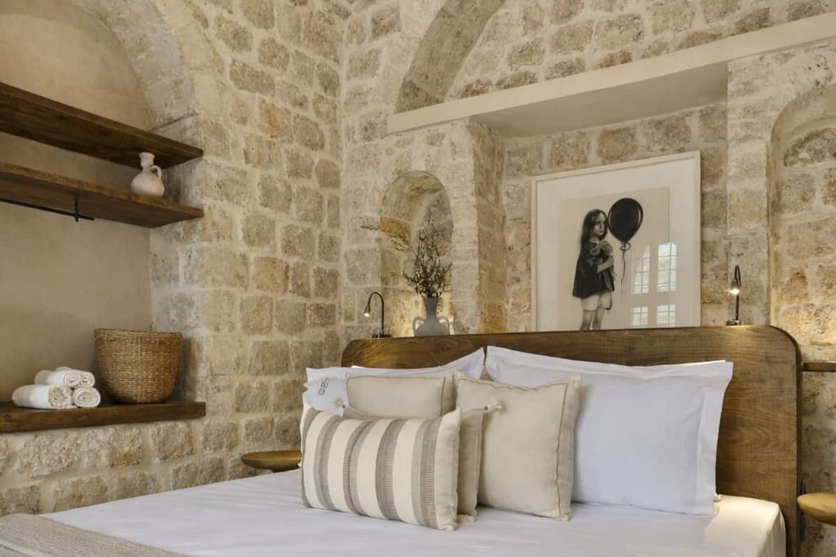 A stone-walled bedroom with a large bed, wooden headboard, and a mirror above it.