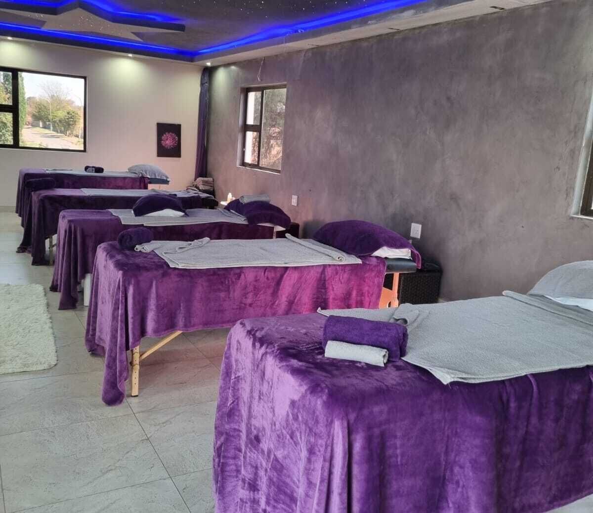 A room with multiple beds covered in purple linens, a large window, and a view of the outdoors.