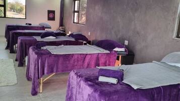 A room with multiple beds covered in purple linens, a large window, and a view of the outdoors.