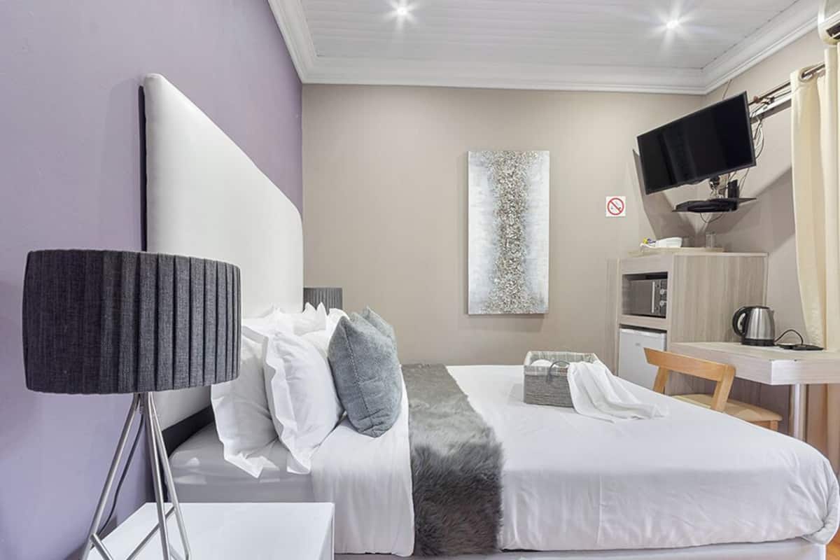 A hotel room with a bed, a desk, a television, and a wall-mounted artwork.
