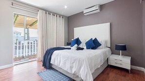 A bedroom with a large bed, a nightstand, a lamp, and a view of the outside. - Botle Ba Afrika Lodge (Vereeniging)