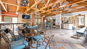 Un'ampia sala da pranzo con soffitto alto e travi a vista in legno, una cucina dotata di elettrodomestici moderni e un'accogliente zona salotto.