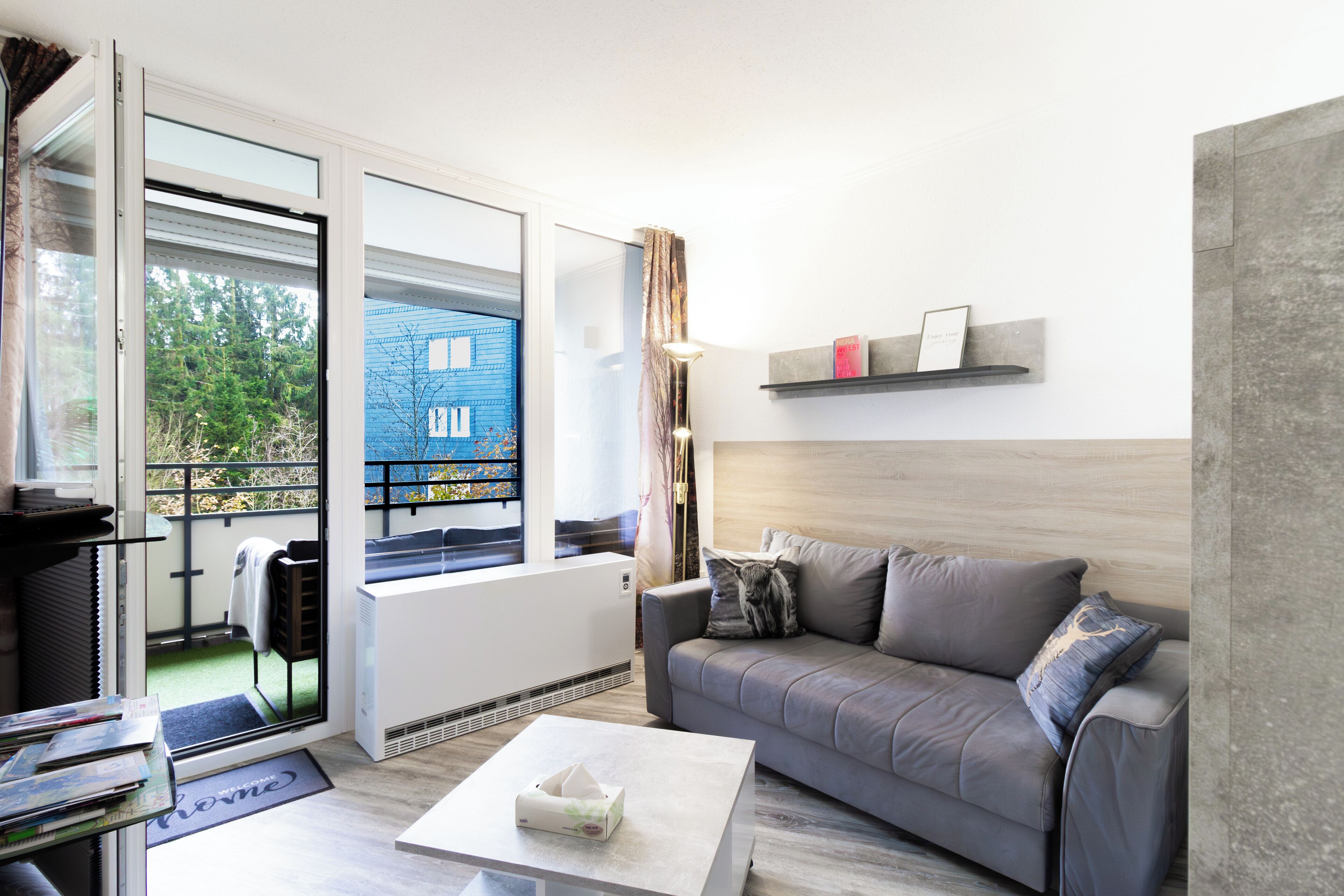 A modern living room with a grey sofa, a coffee table, and a sliding glass door leading to a balcony.