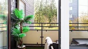 Ein Balkon mit einem Blumentopf, einer Couch und Blick auf Bäume und Gebäude.