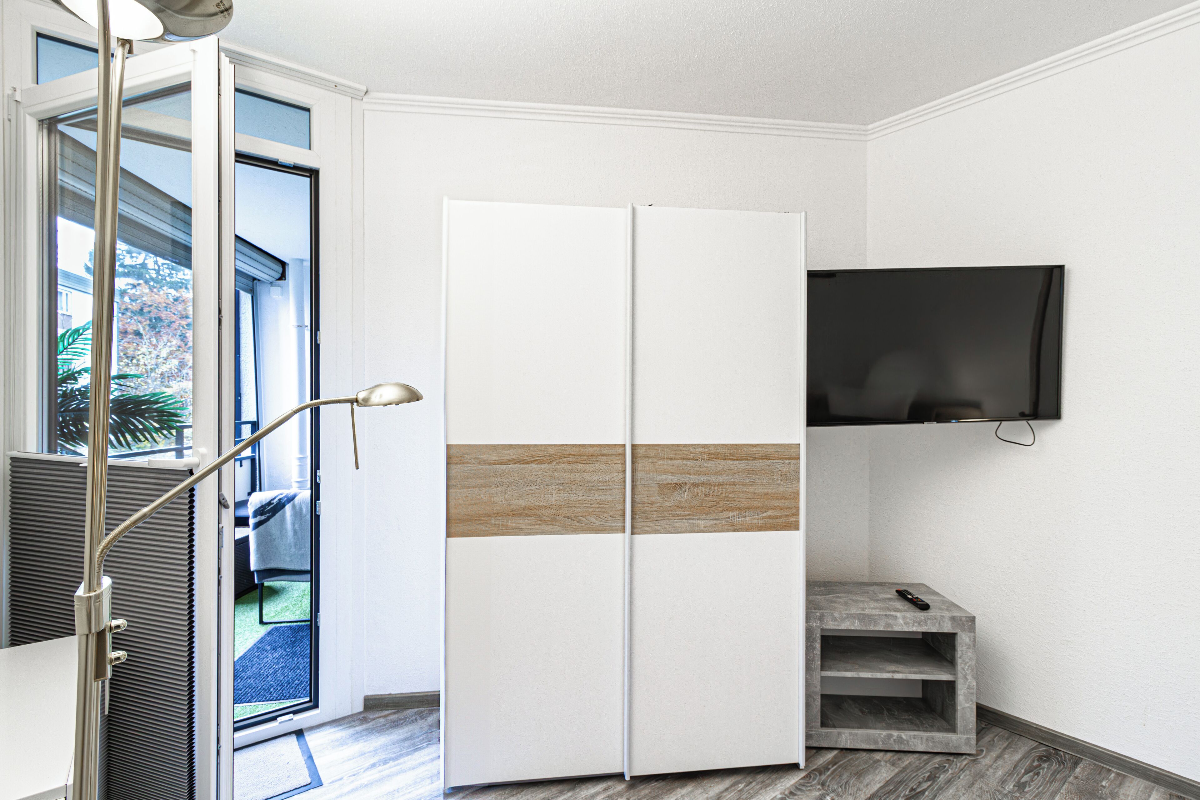 A modern room with a sliding door, a mounted TV, and a small wooden shelf.