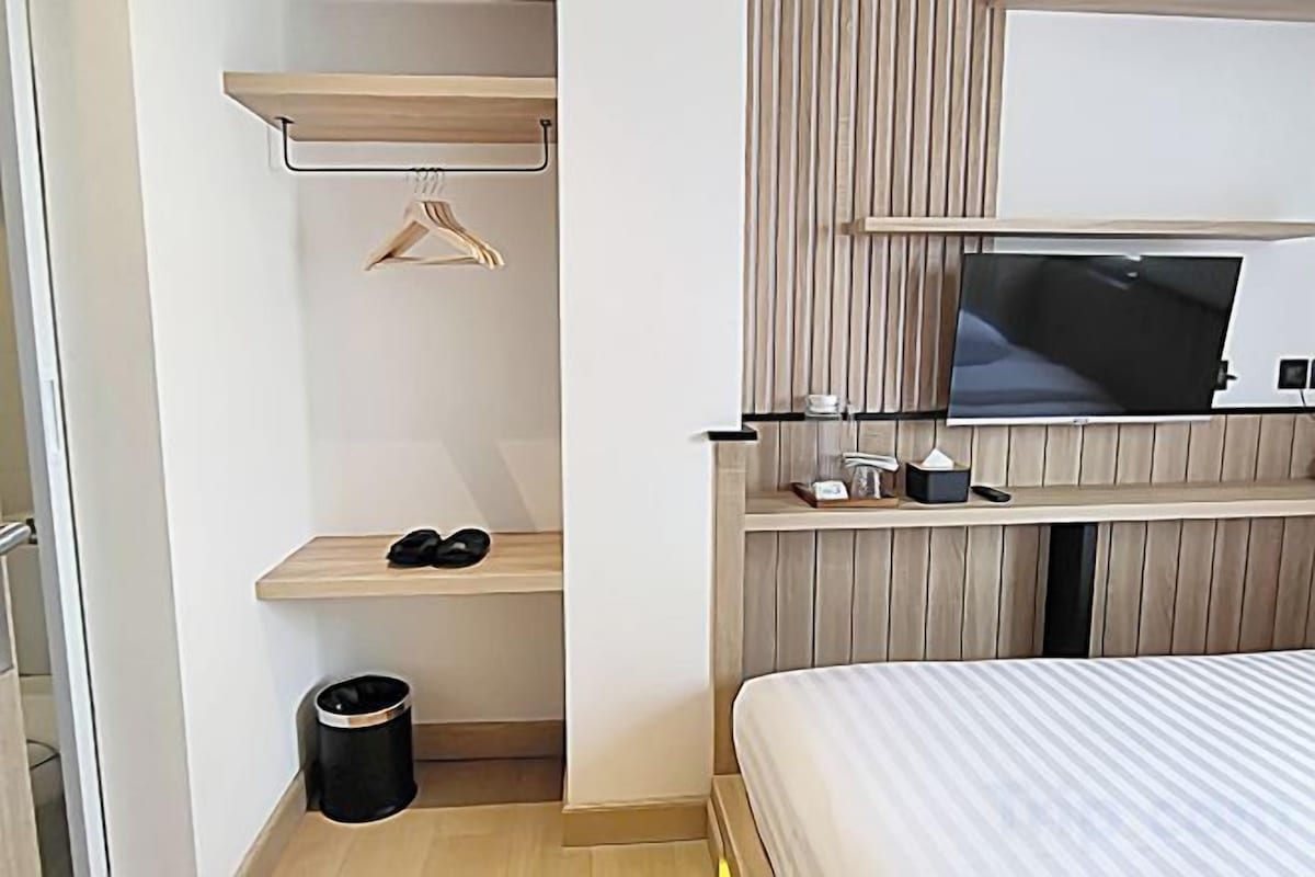Ein Hotelzimmer mit einem Bett, einem Fernseher, einem Schuhregal und einem Mülleimer.