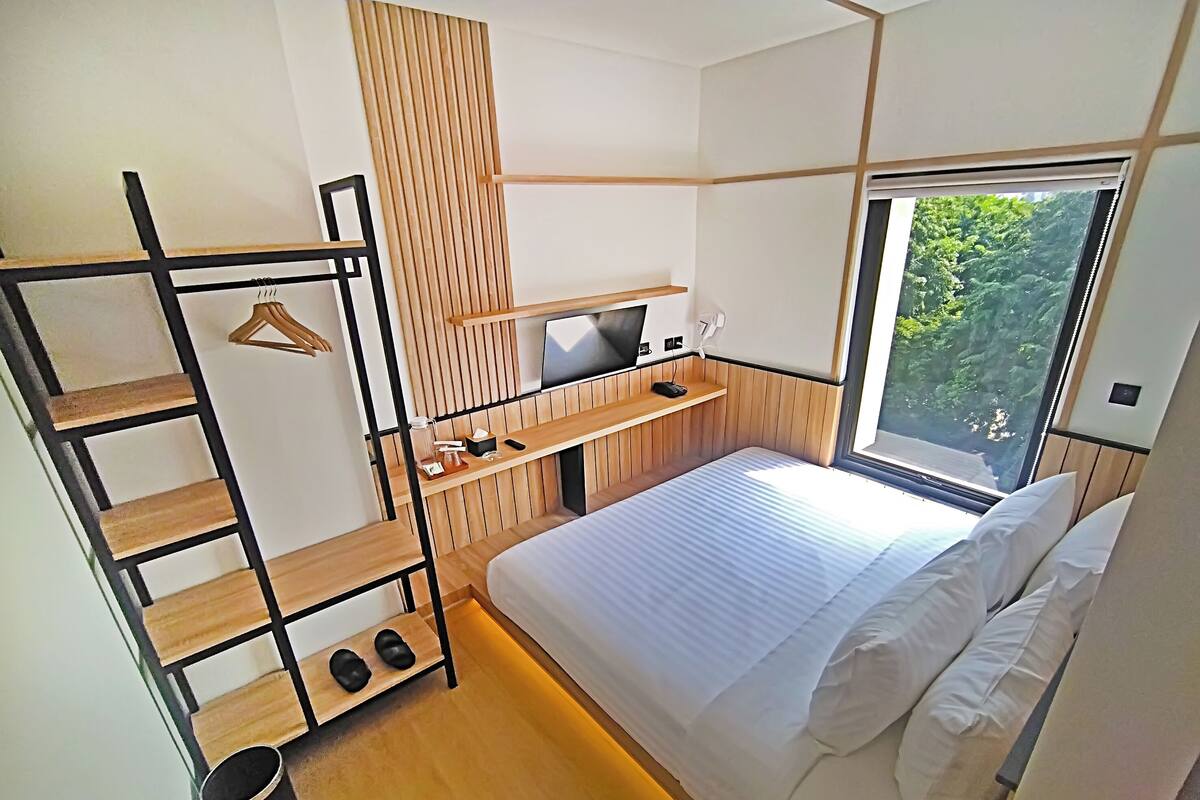A modern bedroom with a bunk bed, a desk with a computer, and a window with a view of greenery.