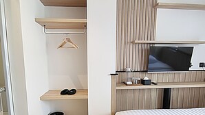 Een moderne hotelkamer met een bed, een aan de muur bevestigde televisie, een klein plankje met een kapstok en een prullenbak.