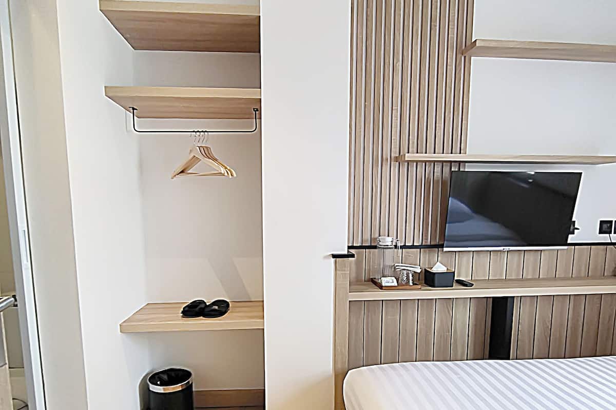 A modern hotel room with a bed, a TV mounted on the wall, a small shelf with a hanger, and a trash bin.