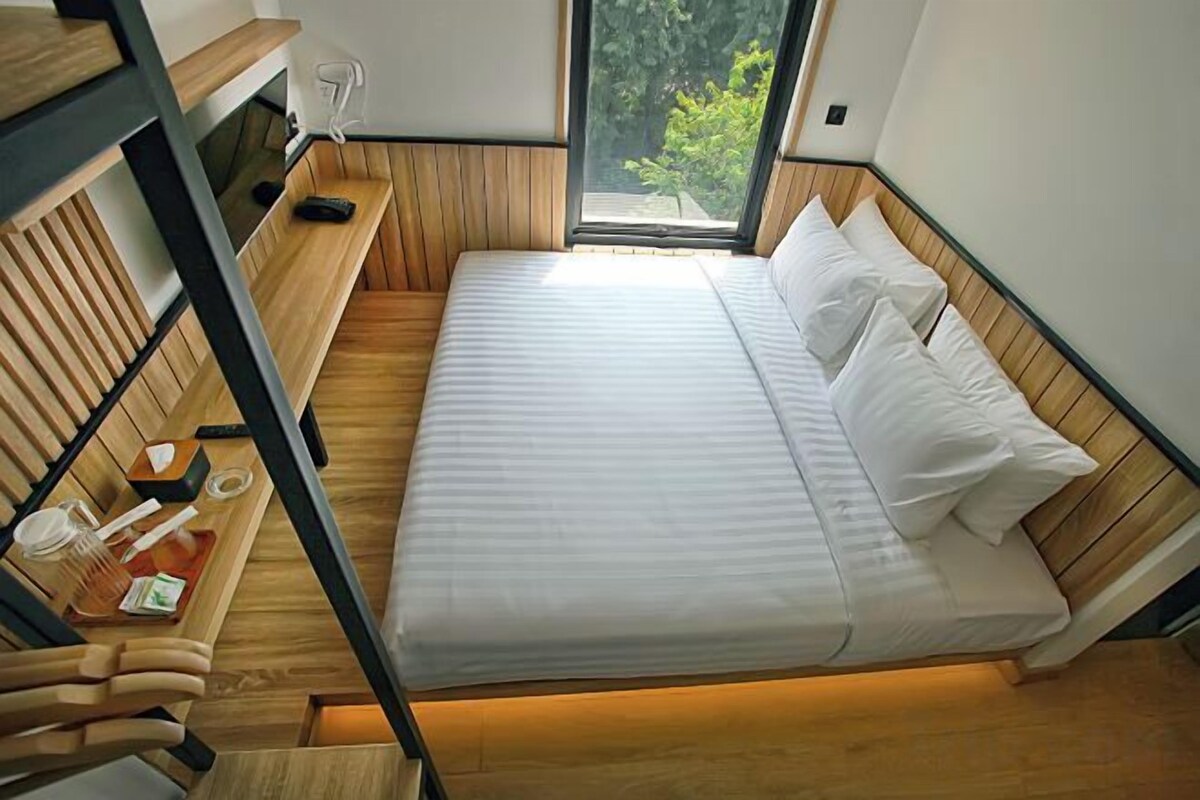 Ein Zimmer mit einem Etagenbett, einem Schreibtisch mit Stuhl und einem Fenster mit Blick auf Grünflächen.