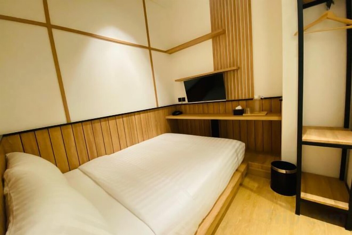 Ein Zimmer mit einem Bett, einem Fernseher, einem Regal und einer Kleiderstange.
